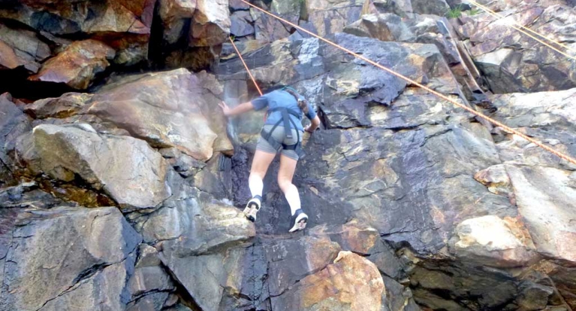 A person wearing safety gear is attached to ropes as they scale a rock wall 